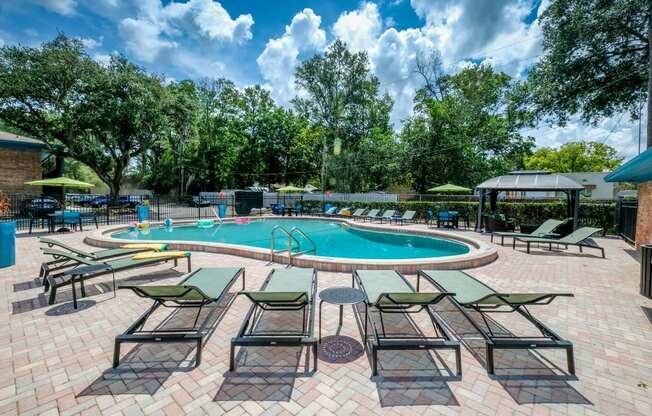 Line of green lounge chairs next to Community pool at the Watermarc Apartments in Lakeland, Fl facing pool and large trees beyond pool fence.