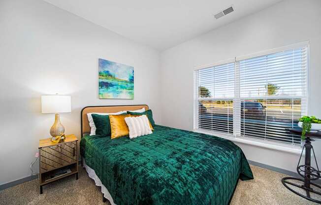 A bedroom with a green bedspread and a painting on the wall.