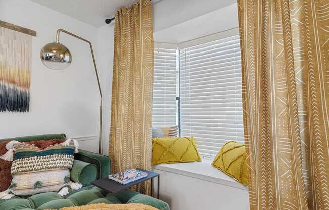 a window seat with yellow curtains and a green sofa