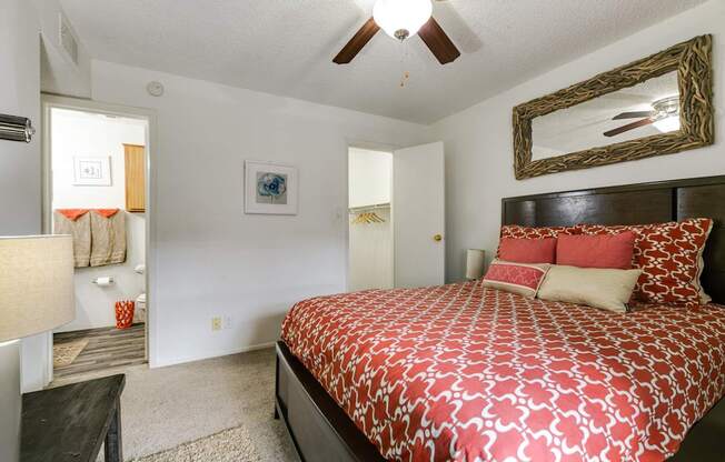 A bedroom with a patterned bedspread and a ceiling fan.