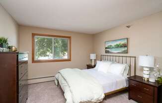 Bedroom with white comforter, and a lamp on the wooden nightstand