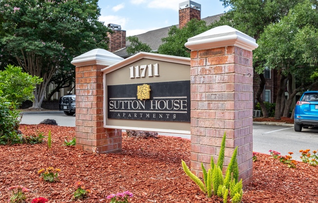 A sign for Sutton House Apartments is displayed in front of a brick wall.