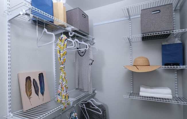 Fusion Las Vegas apartment closet with grey and blue cloth storage boxes, towels, and hangers on built in wire shelving.