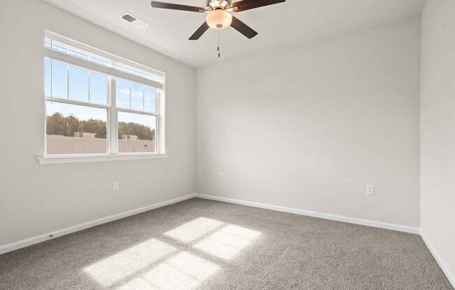 A room with a ceiling fan and a window letting in sunlight.