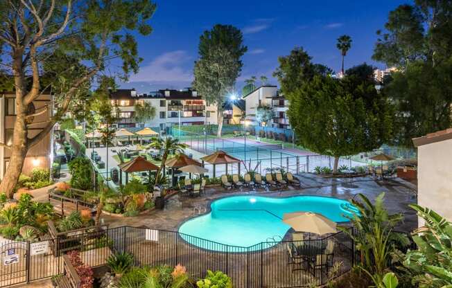 Fusion Warner Center apartments in Woodland Hills pool, courtyard, and tennis courts lit at night and surrounded by palm trees.