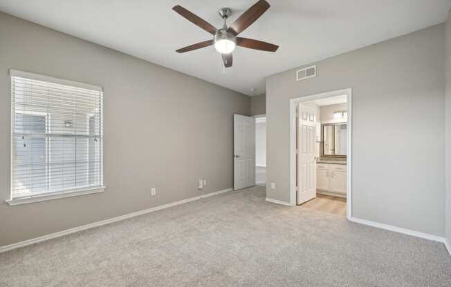 an empty living room with a ceiling fan and a door to a bathroom