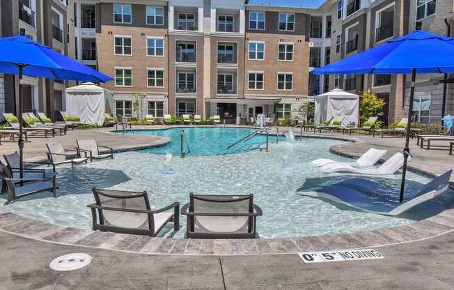 a large pool with chairs and umbrellas in front of an apartment building