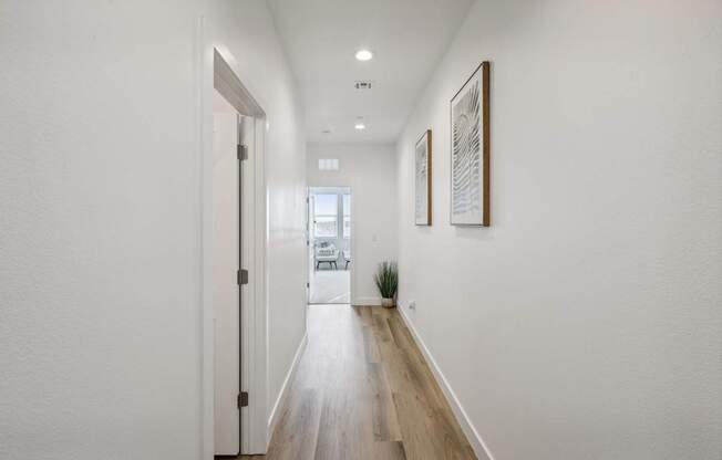 A long hallway with a door on the left and two pictures on the wall.