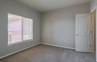 an empty bedroom with a large window and a white door at Stetson Meadows Apartments, Colorado