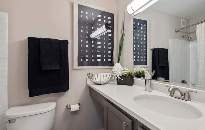 A bathroom with a toilet, sink, mirror, and a black towel hanging on the wall.