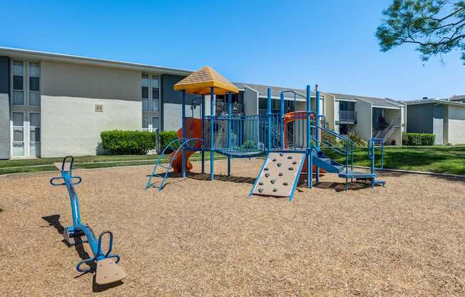 A playground with a blue swing set and a yellow umbrella.