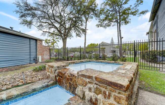 a pool with a stone wall and a fence around it