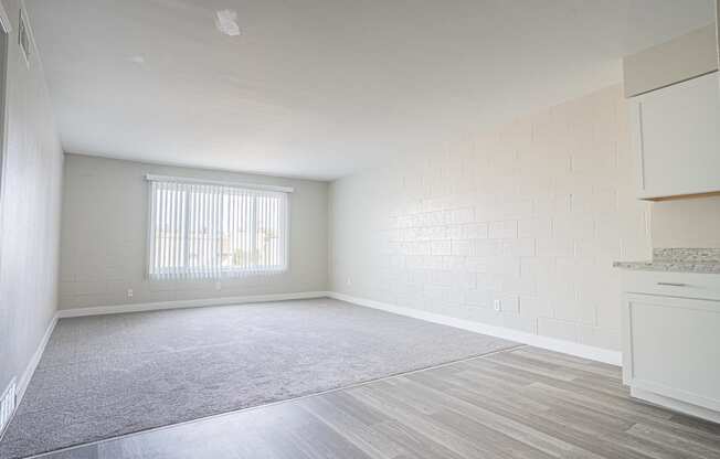 an empty living room with a window and a kitchen