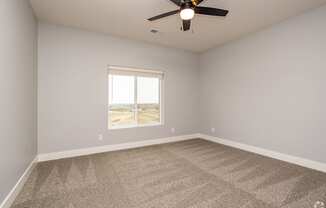 A room with a ceiling fan and a window overlooking a desert landscape.