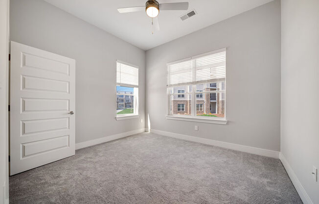 an empty room with a white door and two windows