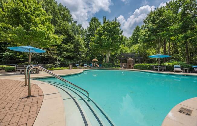 a swimming pool with trees in the background and blue umbrellas