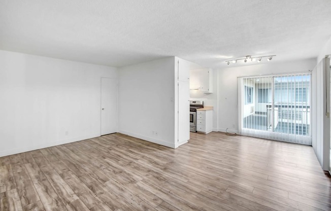 the living room and kitchen of an apartment with hardwood flooring and a balcony