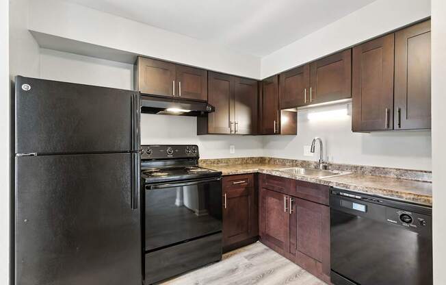 A black refrigerator is in a kitchen with wooden cabinets.