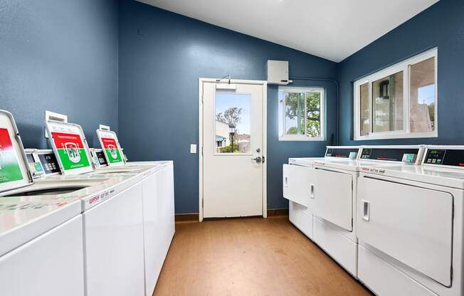 A laundromat with washers and dryers and a view of the outside.