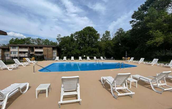 A pool surrounded by white chairs and trees.