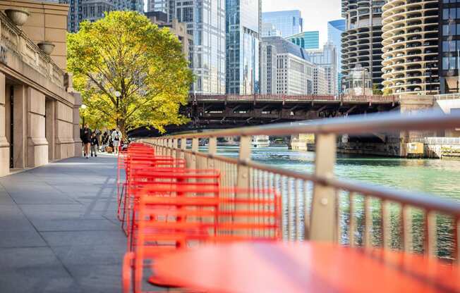 a row of red tables and chairs next to the river in a city