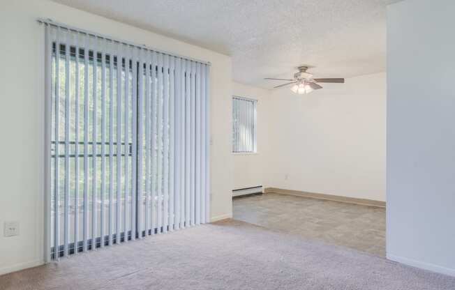 an empty living room with a large window and a ceiling fan