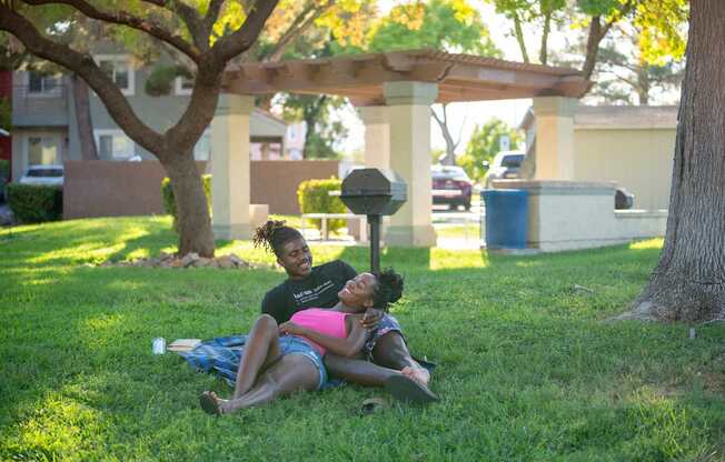 Two people are sitting on the grass under a tree.