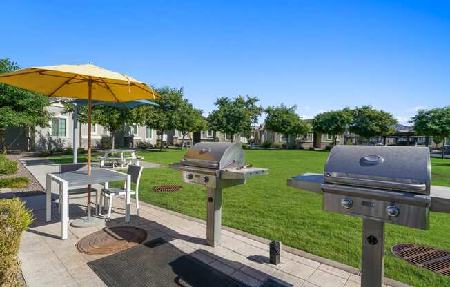 a patio with two bbq grills and a table with an umbrella