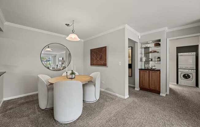 A modern living room with a round table and chairs, a mirror, and a view of the kitchen in the background.