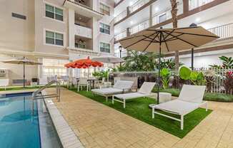 A pool area with a white chair and a brown umbrella.