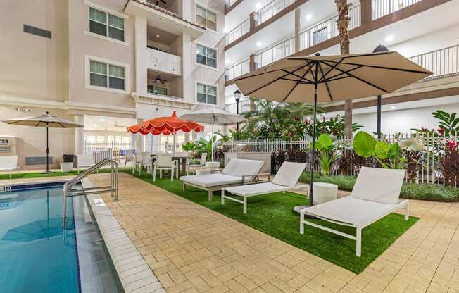 A pool area with a white chair and a brown umbrella.