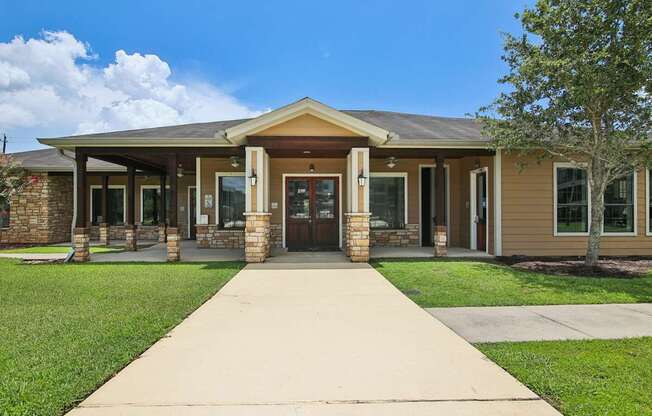 A building with a brown roof and tan walls has a walkway leading to the front door.
