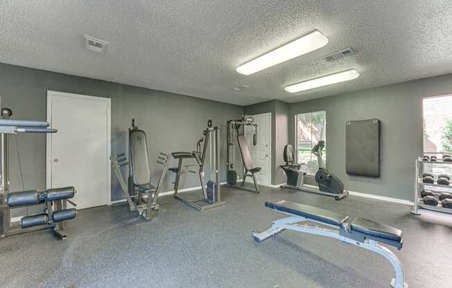 A gym with a variety of equipment including a bench press, a squat rack, and a leg press machine at Copper Hill Apartments, Texas