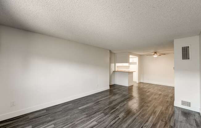 an empty living room and kitchen with wood flooring and a ceiling fan