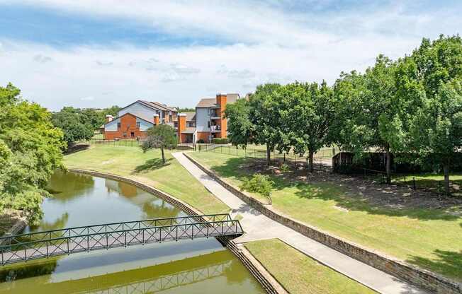 Scenic pond with footbridge, walking path, and open green space beside the community.