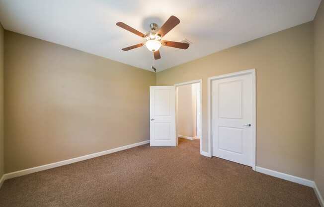 an empty living room with a ceiling fan and two doors