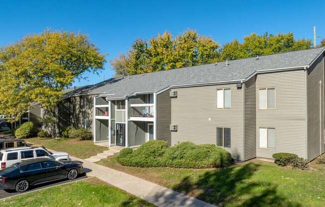 A black car is parked on a driveway in front of a two-story apartment building.