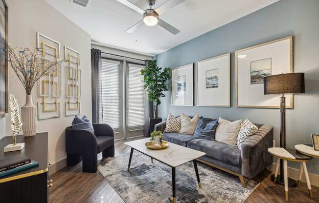 Model apartment living room area with ceiling fan and large window at LynnCora, Grand Prairie, TX, 75052