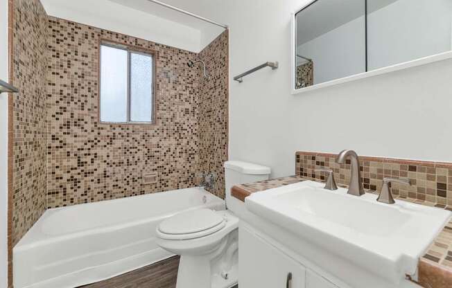 A bathroom with a brown tiled shower and a white sink at The Phoenix Apartments on 6th Avenue, Phoenix, Arizona