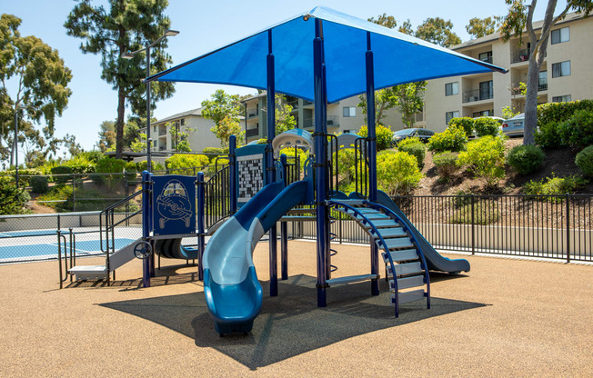 a playground with a blue slide and umbrella in front of a swimming pool