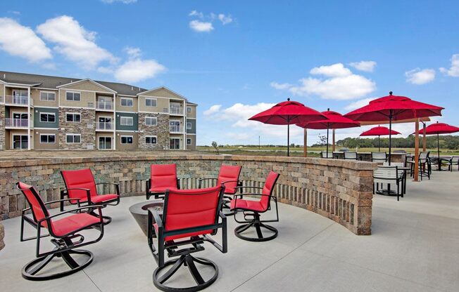 a patio with red chairs and umbrellas at the preserve at great pond apartments in winds