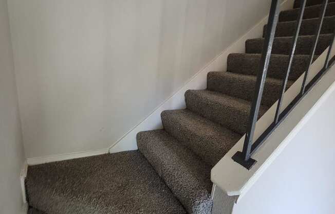 a carpeted staircase with white walls and brown carpeted stairs