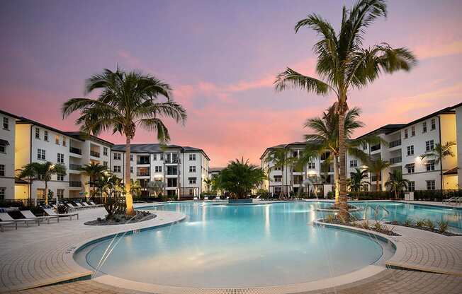 a large swimming pool with palm trees at sunset