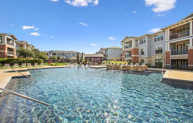 A swimming pool in front of apartment buildings on a sunny day.