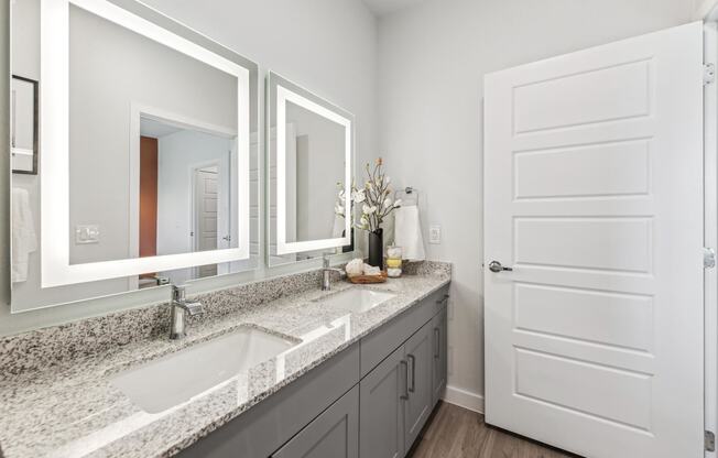 bathroom with back lit mirrors and granite countertops