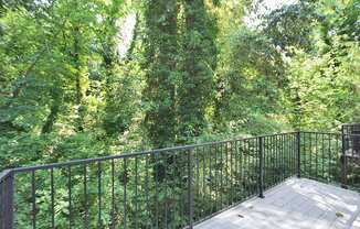 A balcony with a metal railing overlooks a lush green forest.