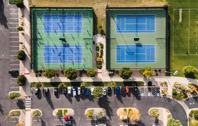 Two tennis courts are surrounded by a parking lot.