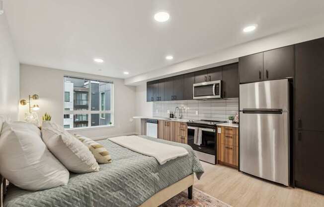 A modern bedroom with a large bed and a kitchen area in the background.