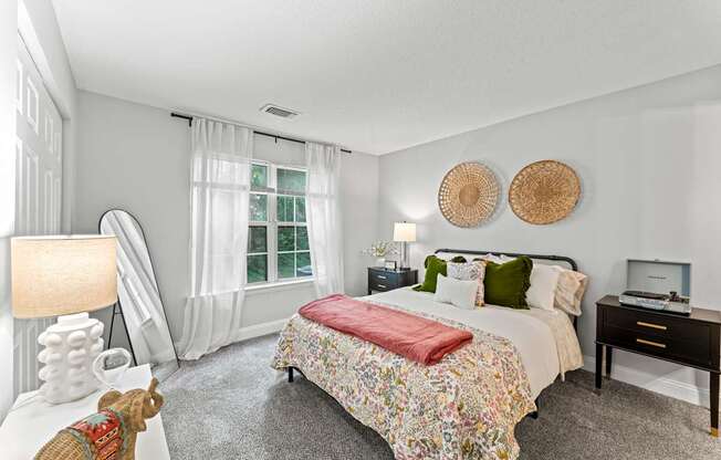 A bedroom with a large bed and a window with white curtains.