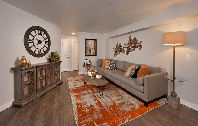 A living room with a grey couch, a wooden cabinet, a clock, and a rug